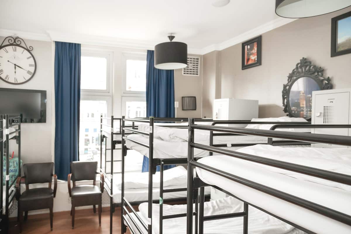 Une chambre de dortoir avec des lits superposés, un bureau, une chaise, un téléviseur et une horloge au mur.