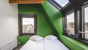 A room with a sloped ceiling, a skylight, a window, and a bed with pillows. - Princess Hostel Amsterdam (Amsterdam)