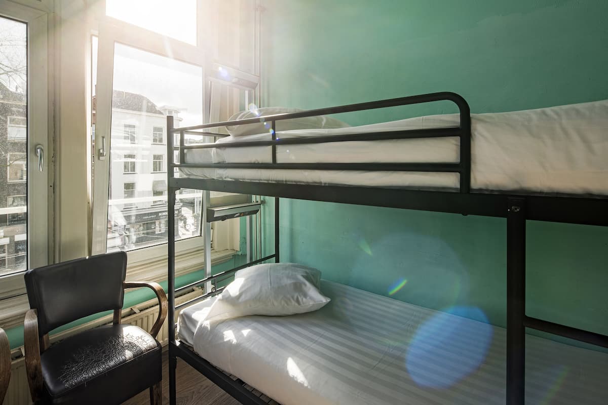 Un lit superposé avec une chaise en bois et une fenêtre donnant sur des immeubles.
