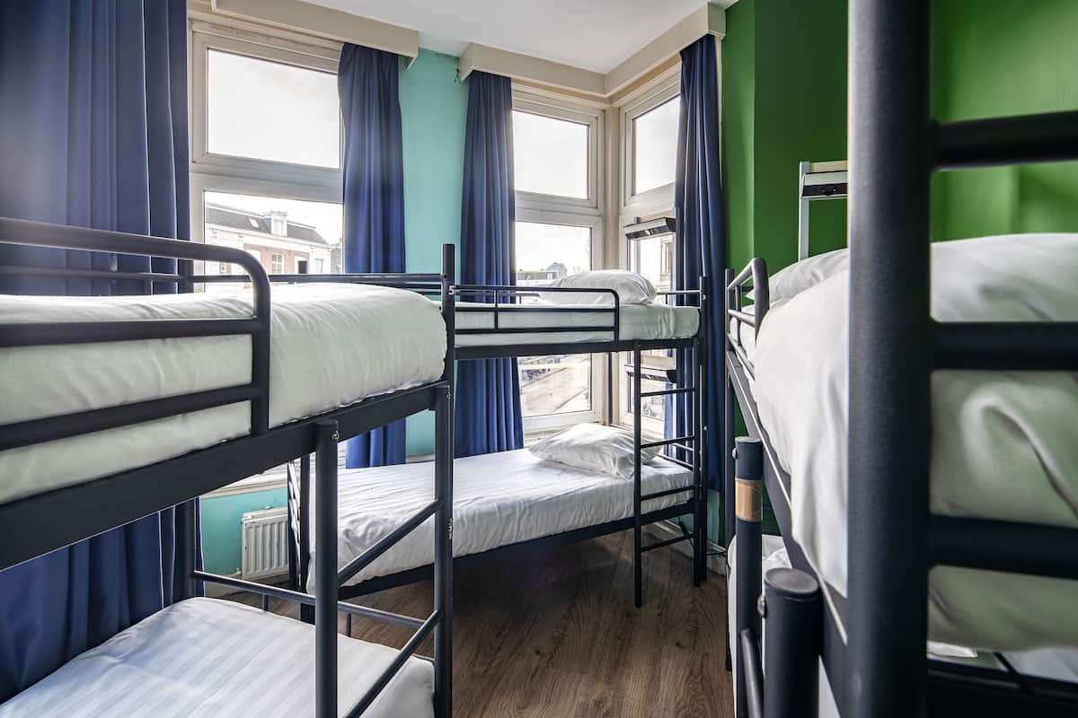 Une chambre de dortoir avec des lits superposés, une fenêtre avec des rideaux et un radiateur.