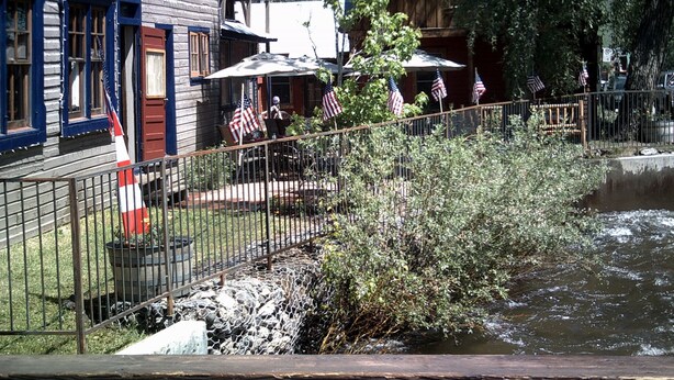 Un bâtiment rustique en bois, doté d’un porche, de drapeaux américains et d’un petit étang.