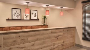 A reception area with a wooden reception desk, framed artwork on the wall, and pendant lighting. - Country Inn & Suites by Radisson, Valparaiso, IN (Valparaiso)