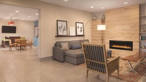 A modern living room with a fireplace, a sofa, a wooden chair, and a dining area with a table and chairs. - Country Inn & Suites by Radisson, Valparaiso, IN (Valparaiso)