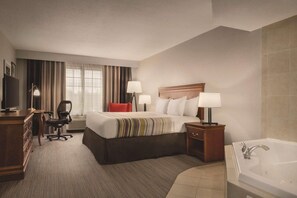 A hotel room with a large bed, two bedside tables with lamps, a desk with a chair, a TV, and a bathroom with a bathtub.