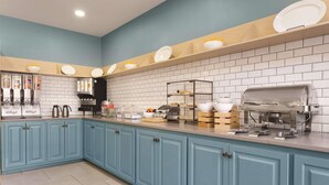 A modern kitchen with blue cabinets, a coffee station, and a buffet area with various food items. - Country Inn & Suites by Radisson, Valparaiso, IN (Valparaiso)