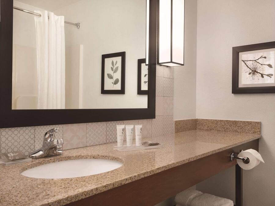 A bathroom with a large mirror, a sink, a towel rack, and framed artwork on the wall.