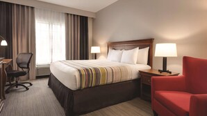A hotel room with a large bed, two bedside lamps, a desk with a chair, and a red armchair. - Country Inn & Suites by Radisson, Valparaiso, IN (Valparaiso)