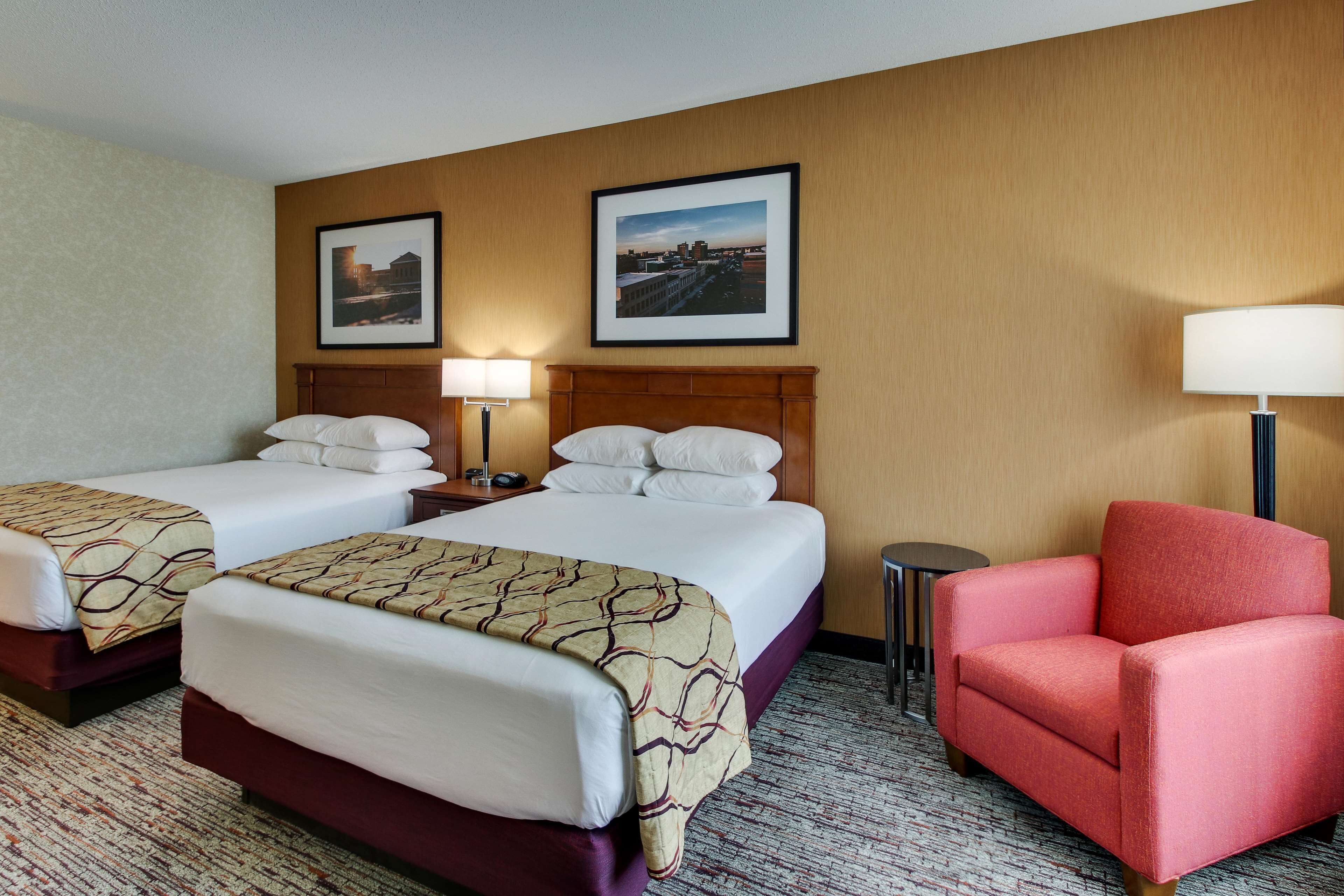 Quarto de hotel com duas camas, uma poltrona vermelha e duas molduras na parede.