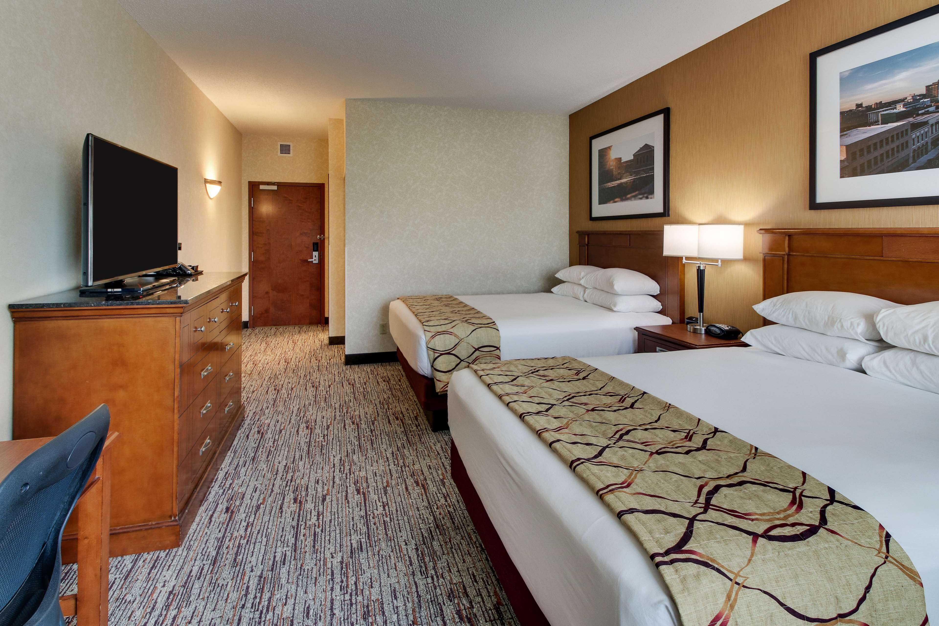 A hotel room with two beds, a desk with a chair, a television, and a door leading to another room.