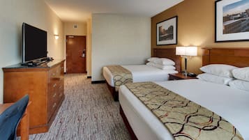 A hotel room with two beds, a desk with a chair, a television, and a door leading to another room.