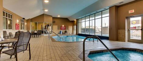 An indoor swimming pool with a 3ft depth marking, surrounded by seating areas and a view of the city.