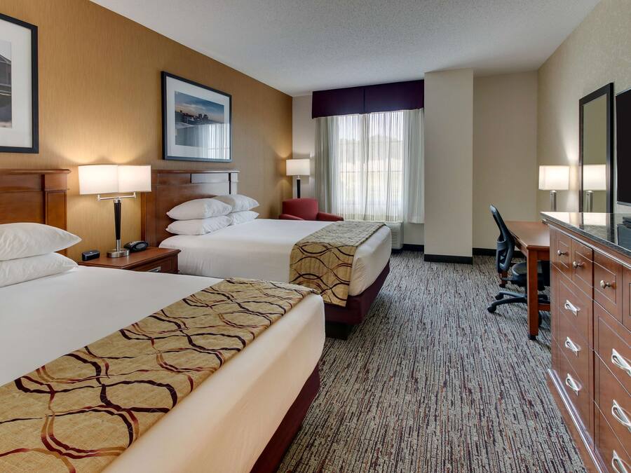 A hotel room with two beds, a desk, a dresser, and a large mirror.