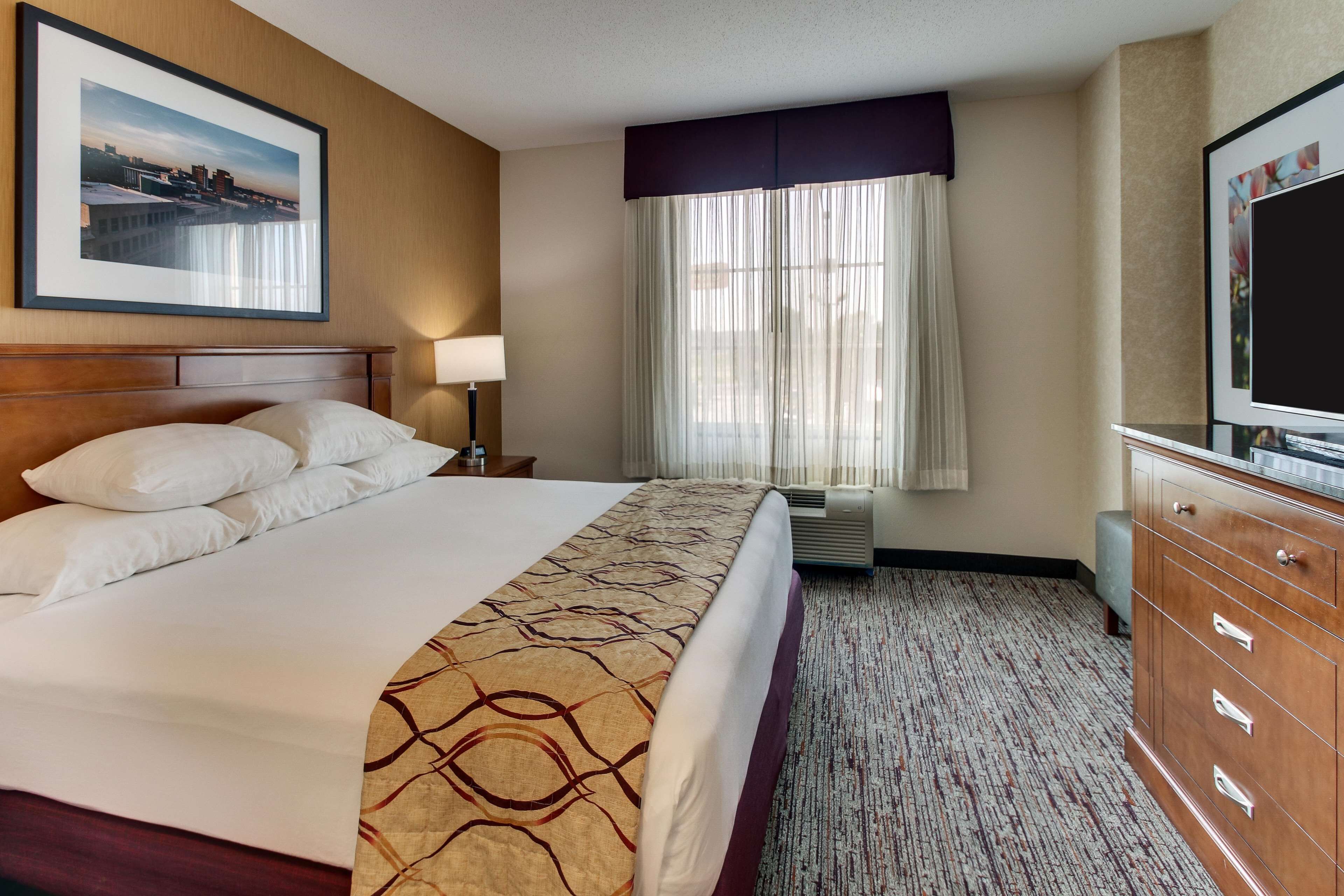 Una habitación de hotel con una cama grande, televisión, cómoda y ventana con cortinas.