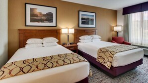 A hotel room with two beds, a wooden headboard, a red chair, and two framed pictures on the wall. - Drury Inn & Suites Meridian (Meridian)