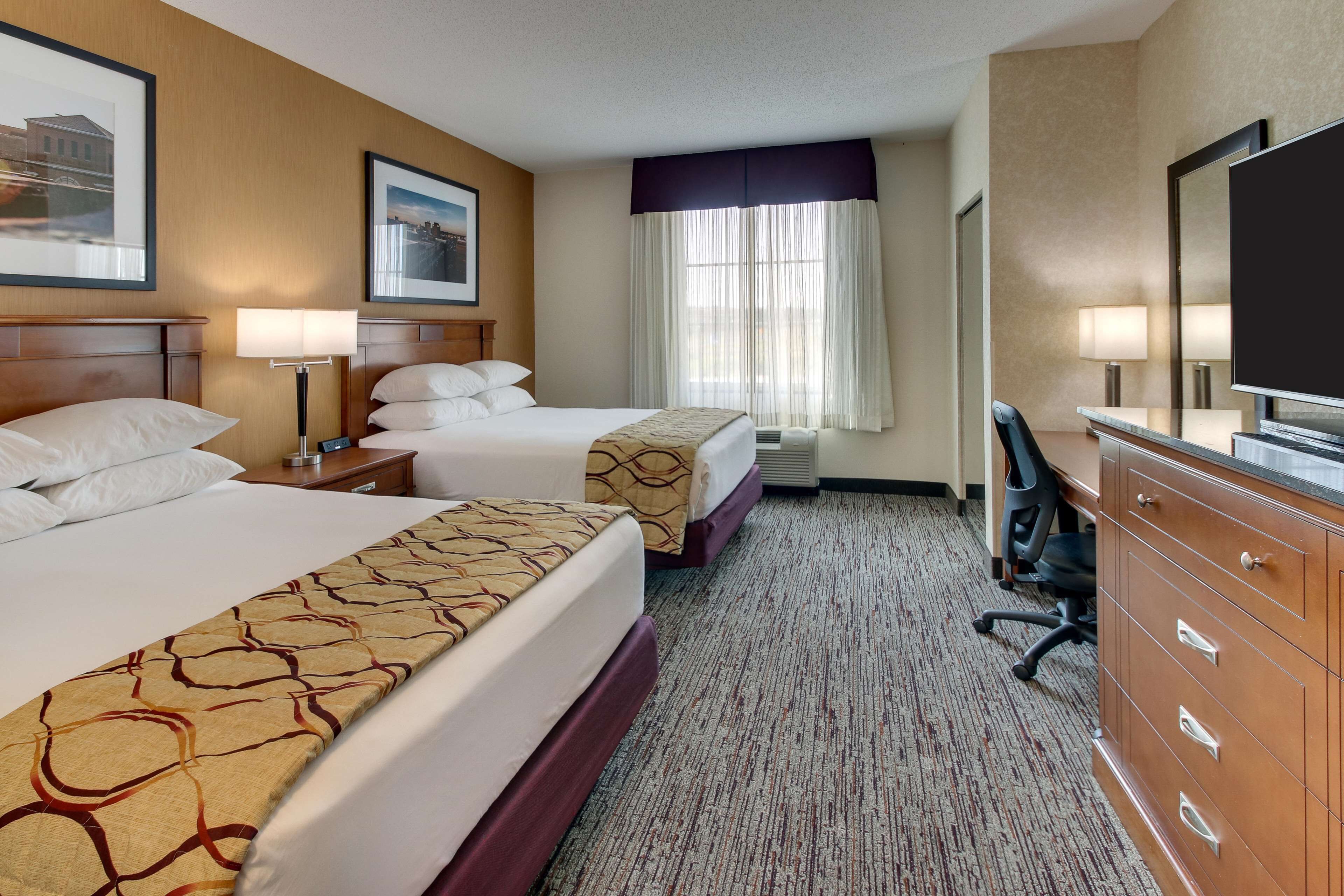 A hotel room with two beds, a desk, a chair, a dresser, and a television.