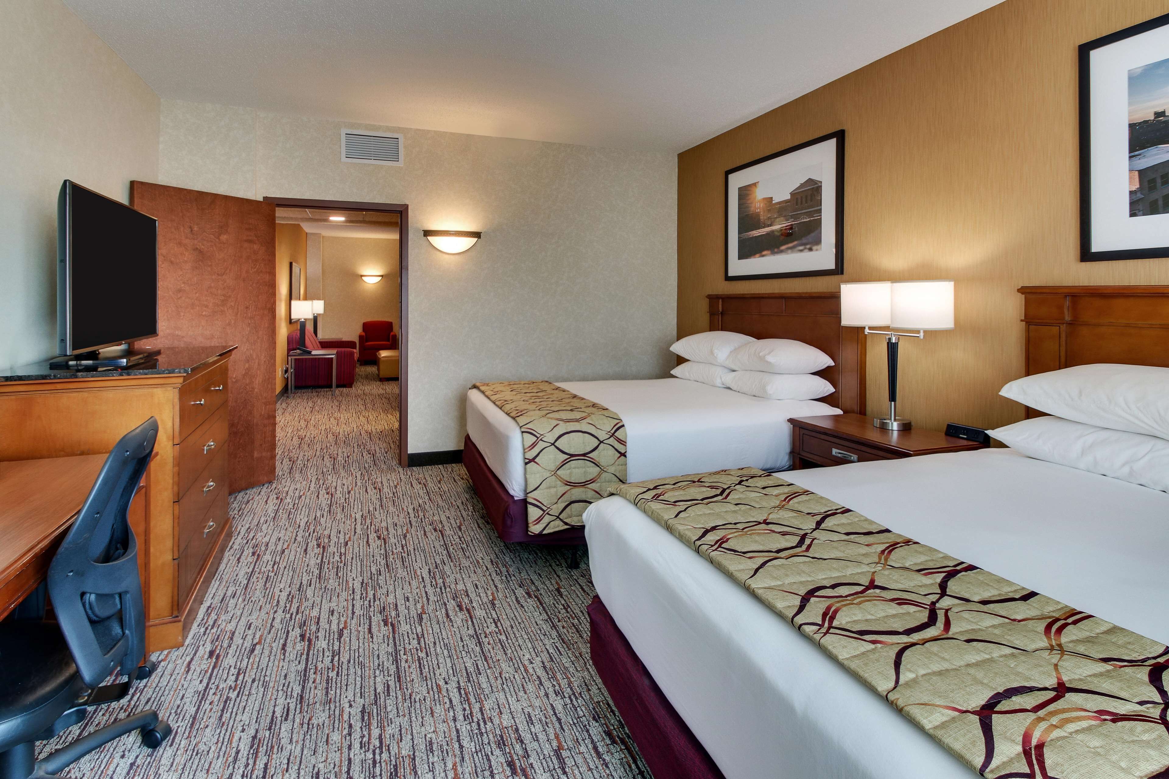 A hotel room with two beds, a desk with a chair, a TV, and a lamp.