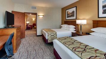 A hotel room with two beds, a desk with a chair, a TV, and a lamp.