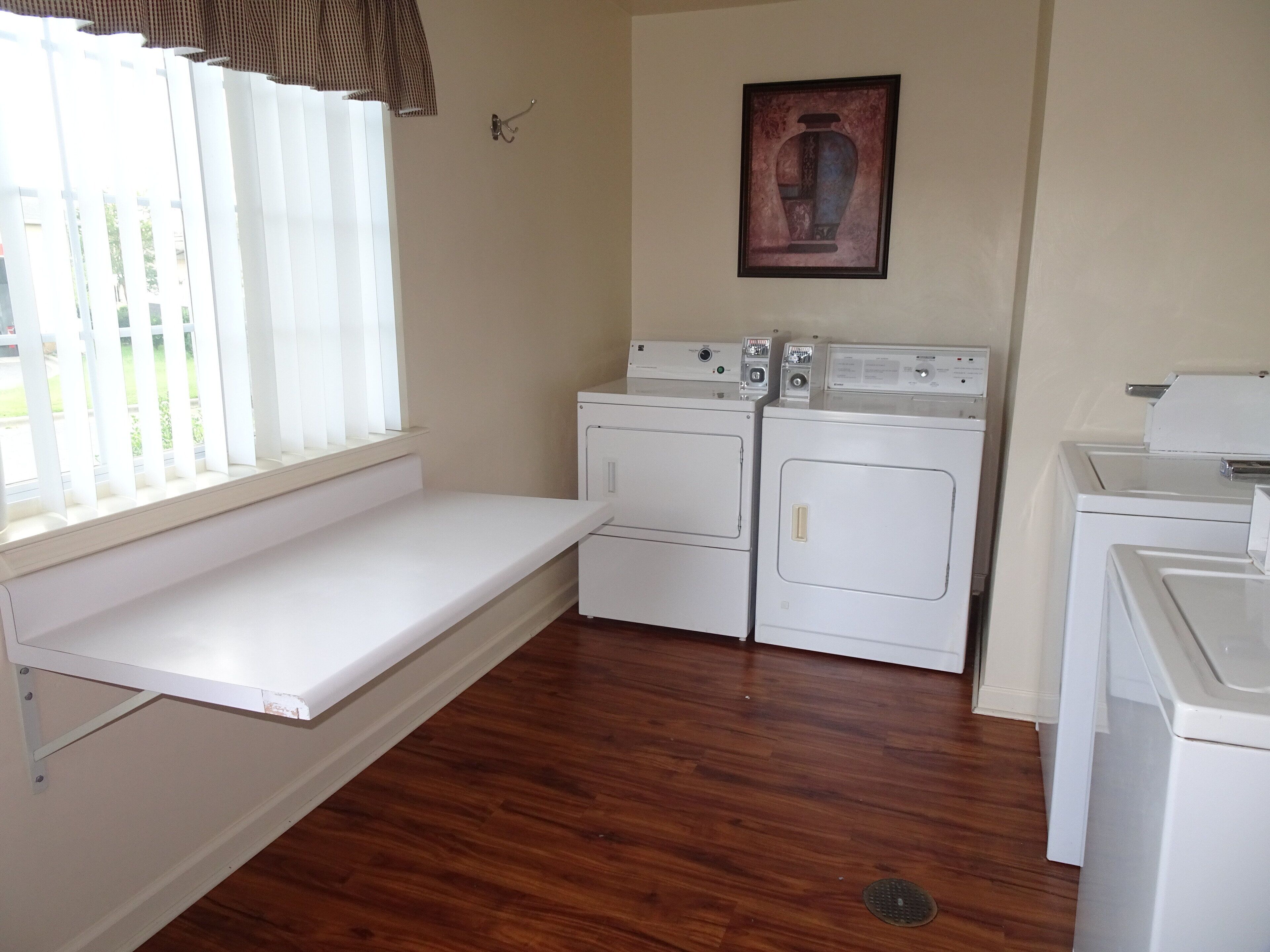 A laundry room with two stacked washers and dryers, a bench under a window, and a wall-mounted picture.