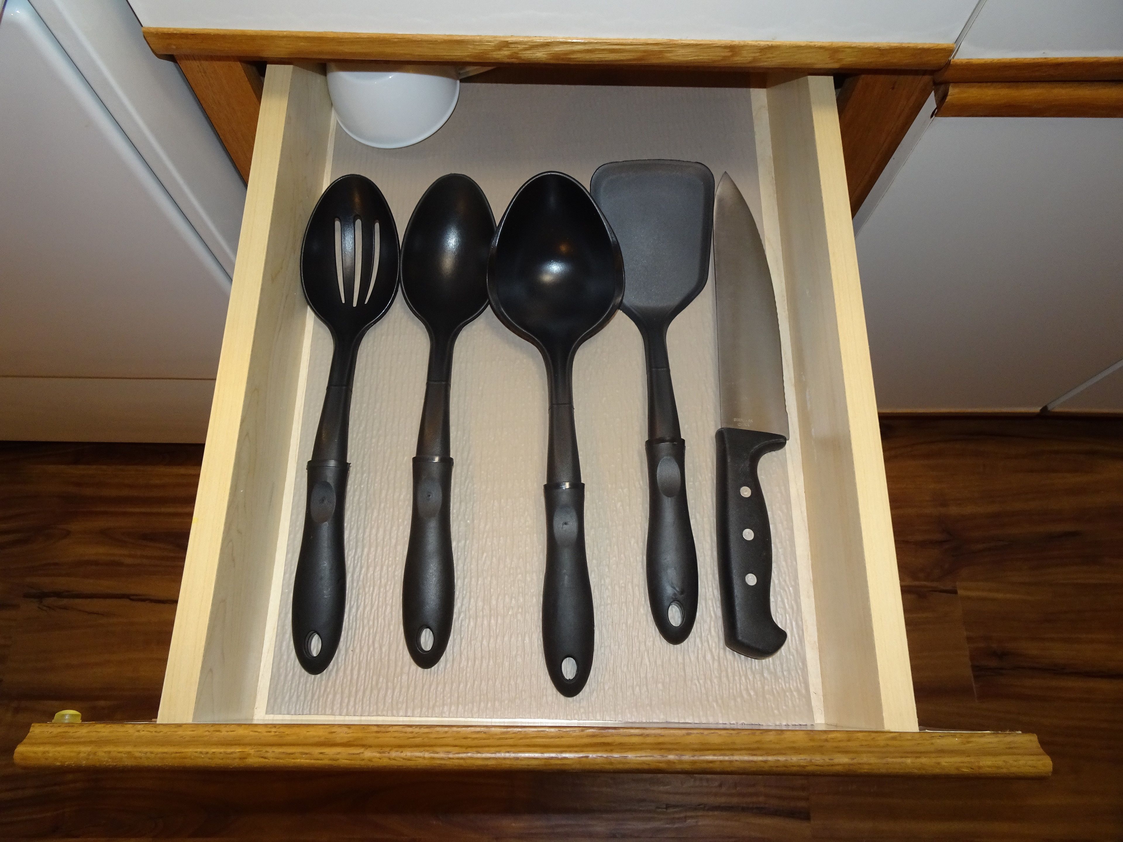 A drawer containing various kitchen utensils including a spatula, a spoon, and a knife.