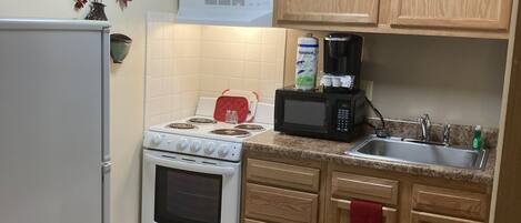 Une cuisine de taille réduite, dotée de meubles en bois, d’un réfrigérateur blanc, d’une cuisinière, d’un four à micro-ondes et d’un évier.