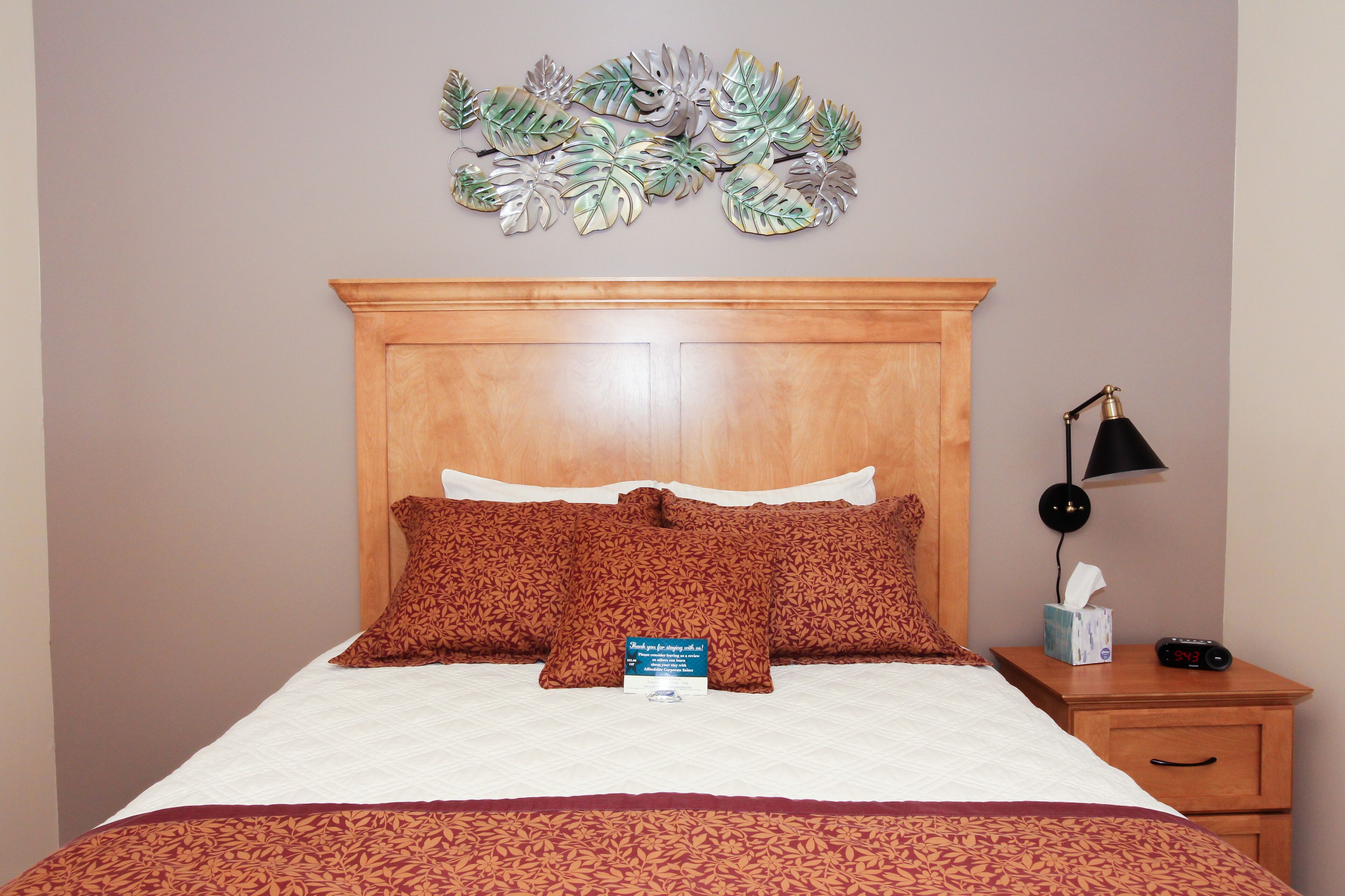 A neatly made bed with a wooden headboard, a bedside table with a lamp, and a wall decoration above the bed.