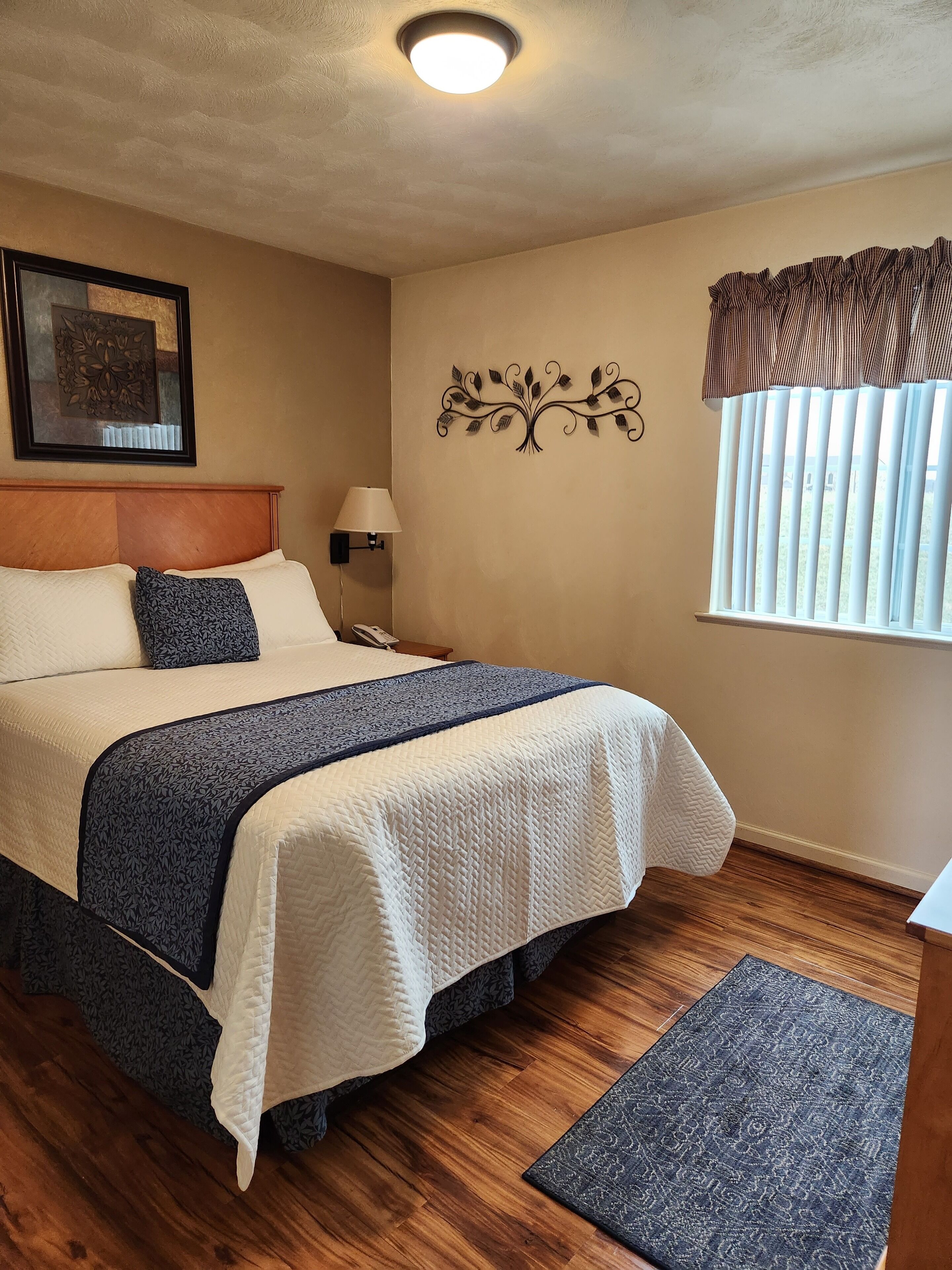 A neatly arranged bedroom with a bed, bedside table, lamp, and a decorative wall piece.