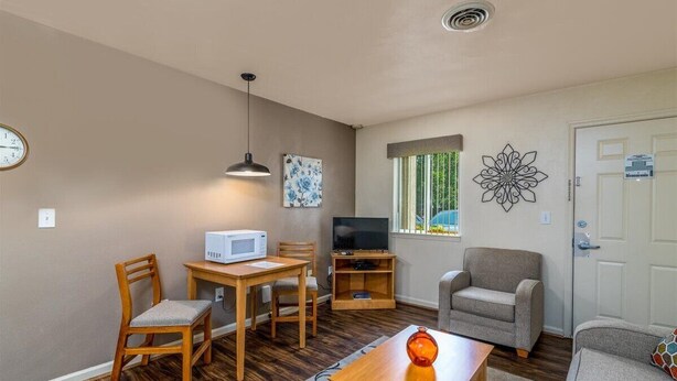 Un espace de vie compact comprenant une table à manger, des chaises, un canapé, un téléviseur et un élément décoratif mural.
