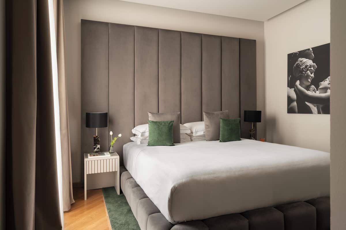 A modern bedroom with a large bed, a headboard, bedside tables, and a wall-mounted artwork.