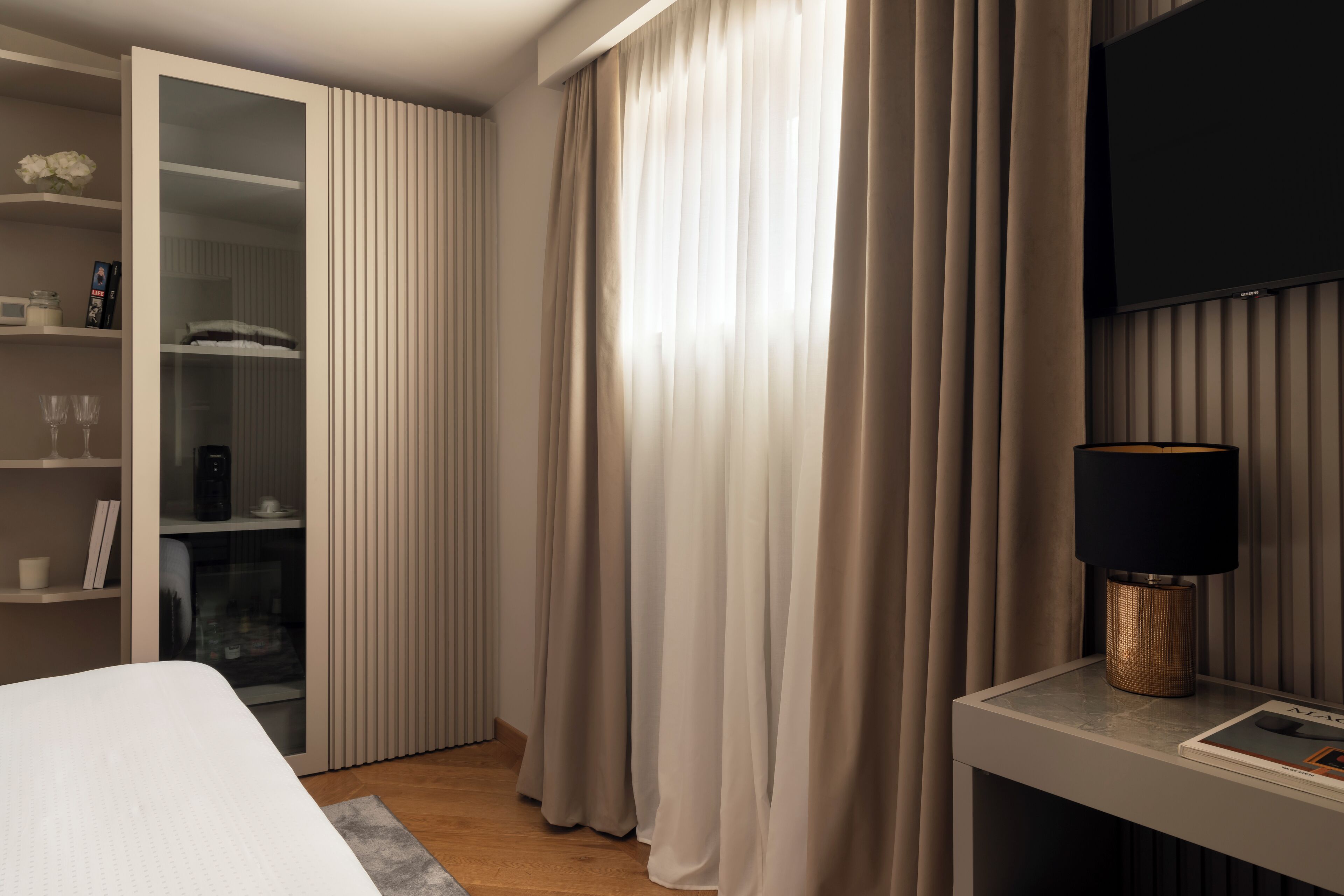 Habitación de hotel moderna con una cama, una mesita de noche con lámpara, un televisor montado en la pared y un armario con puerta corredera.