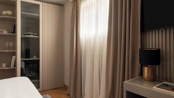 Habitación de hotel moderna con una cama, una mesita de noche con lámpara, un televisor montado en la pared y un armario con puerta corredera.