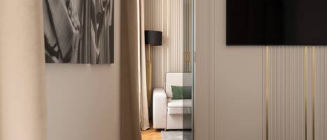 A hotel room with a bed, a flat-screen TV mounted on the wall, a white sofa with a green pillow, and a floor lamp.