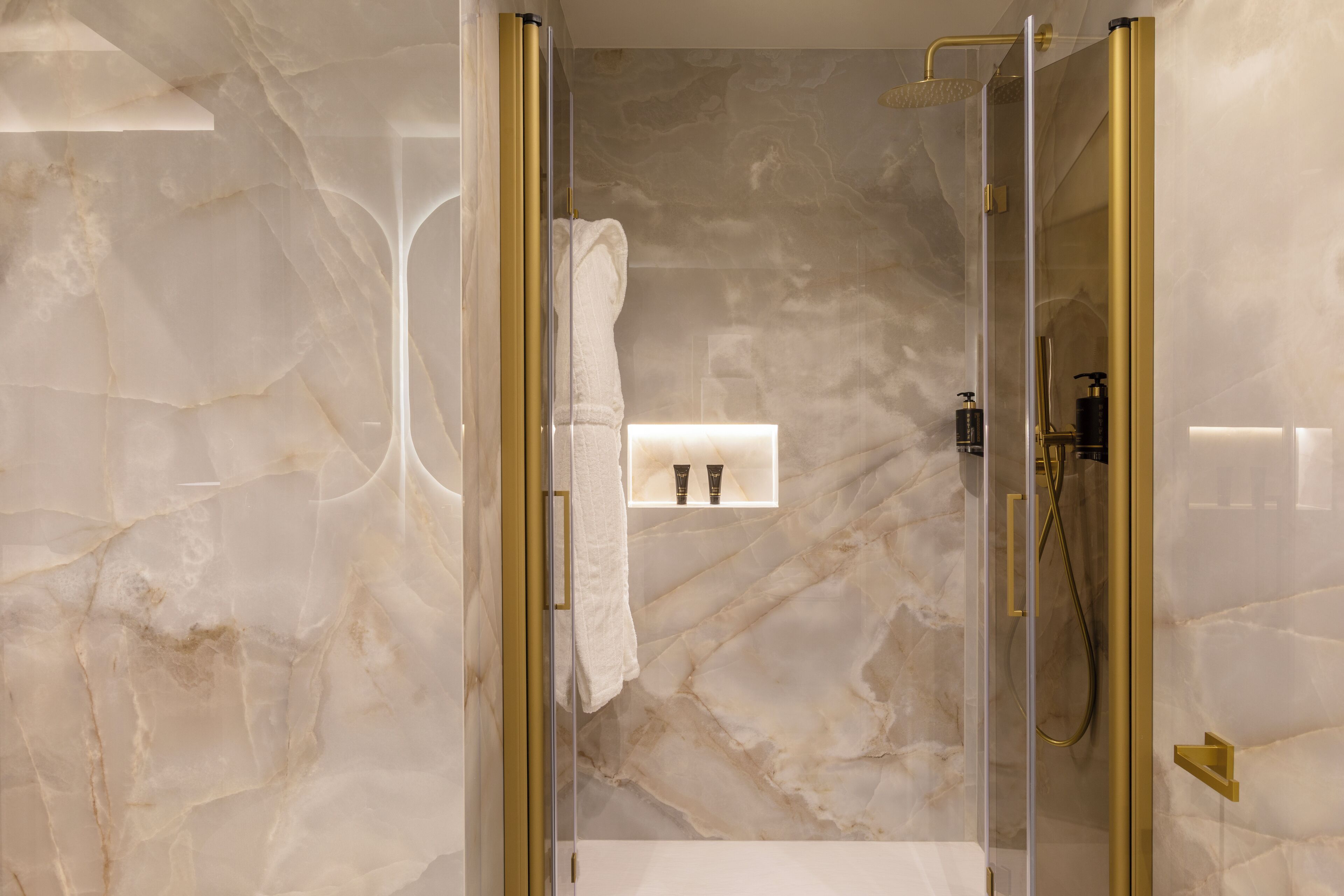 Un baño moderno con ducha envuelta en cristal, paredes de mármol y un perchero para toallas.