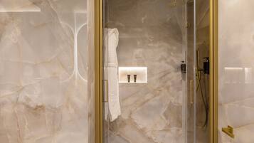Un baño moderno con ducha envuelta en cristal, paredes de mármol y un perchero para toallas.