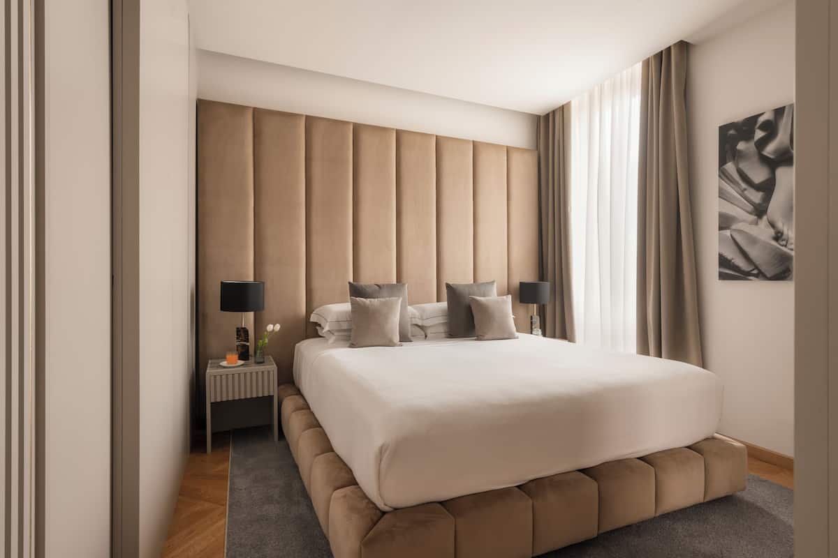 A modern bedroom with a large bed, a nightstand, and a wall-mounted lamp.