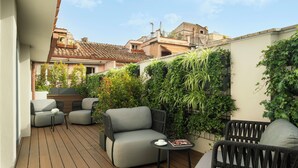 Una terraza en la azotea con mobiliario exterior, una mesa pequeña y una pared cubierta de follaje.