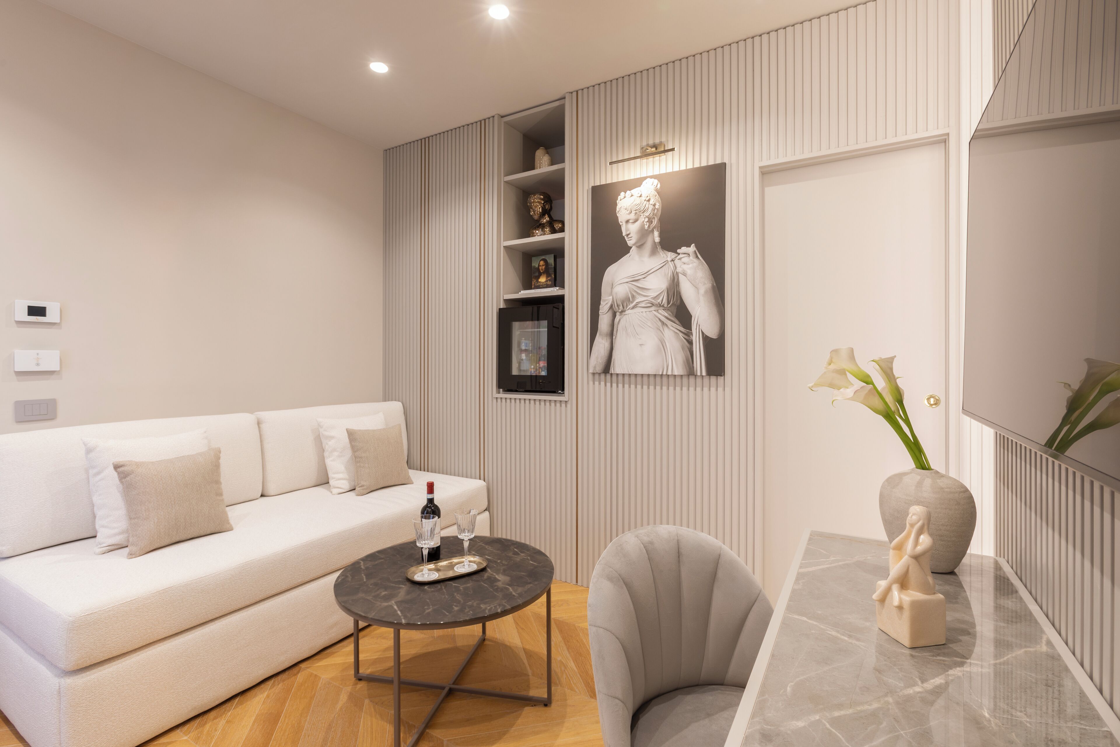 Una sala de estar moderna con un sofá blanco, una mesa de centro redonda, una mesita auxiliar de mármol y una estatua.