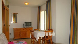 A dining area with a table, chairs, a television on a cabinet, and a sofa with a quilt.