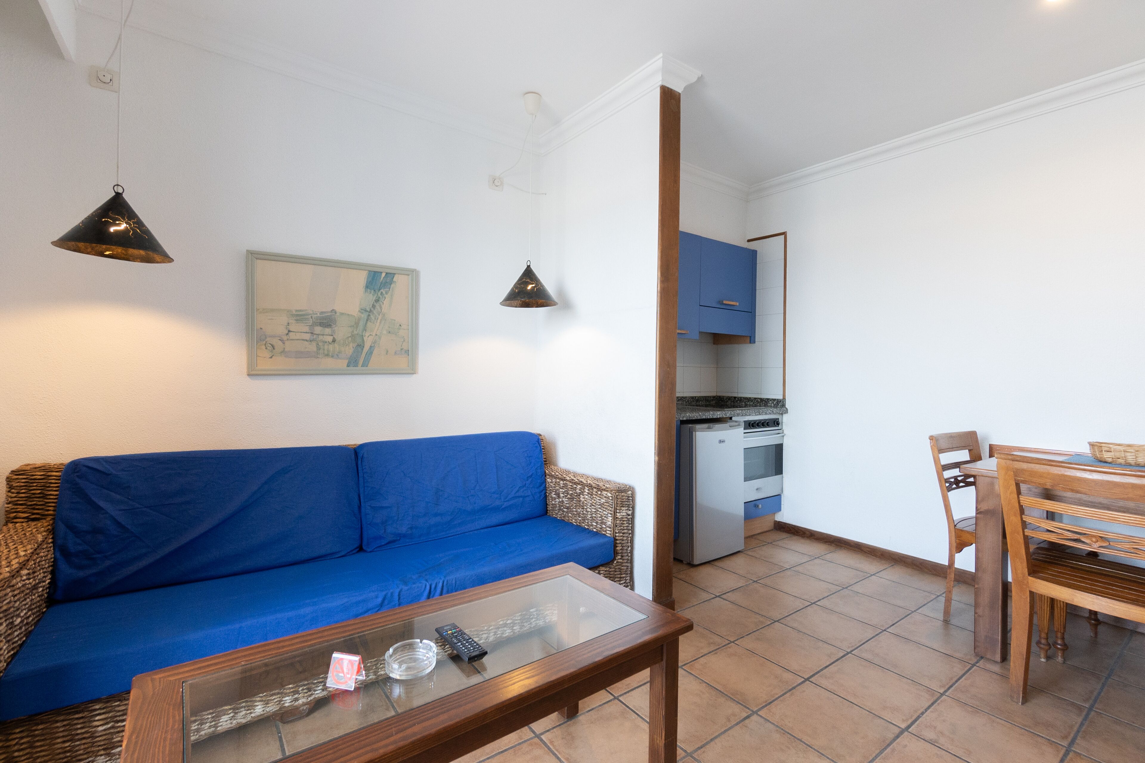 Un salón con un sofá azul, una mesa de centro de vidrio y una zona de comedor con sillas y una mesa de madera.