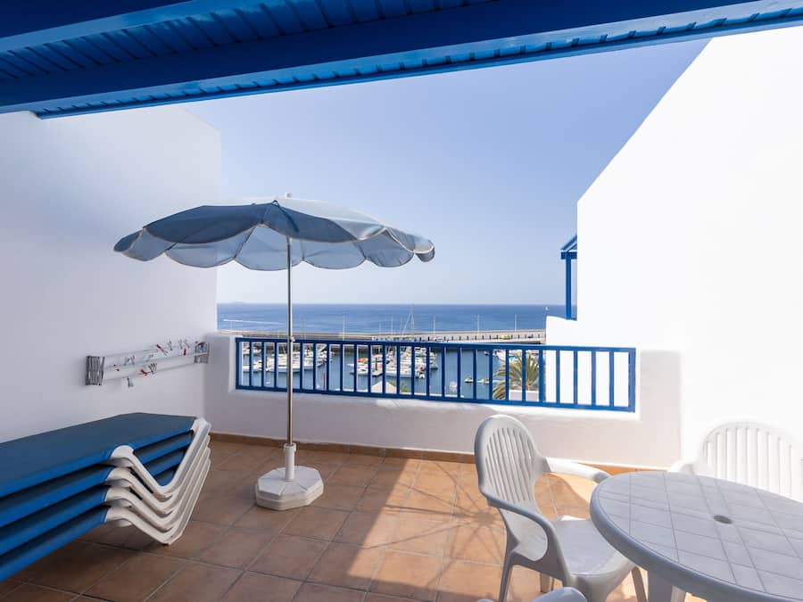 A balcony with a blue ceiling, white walls, a white table with chairs, a white bench, and a white umbrella.
