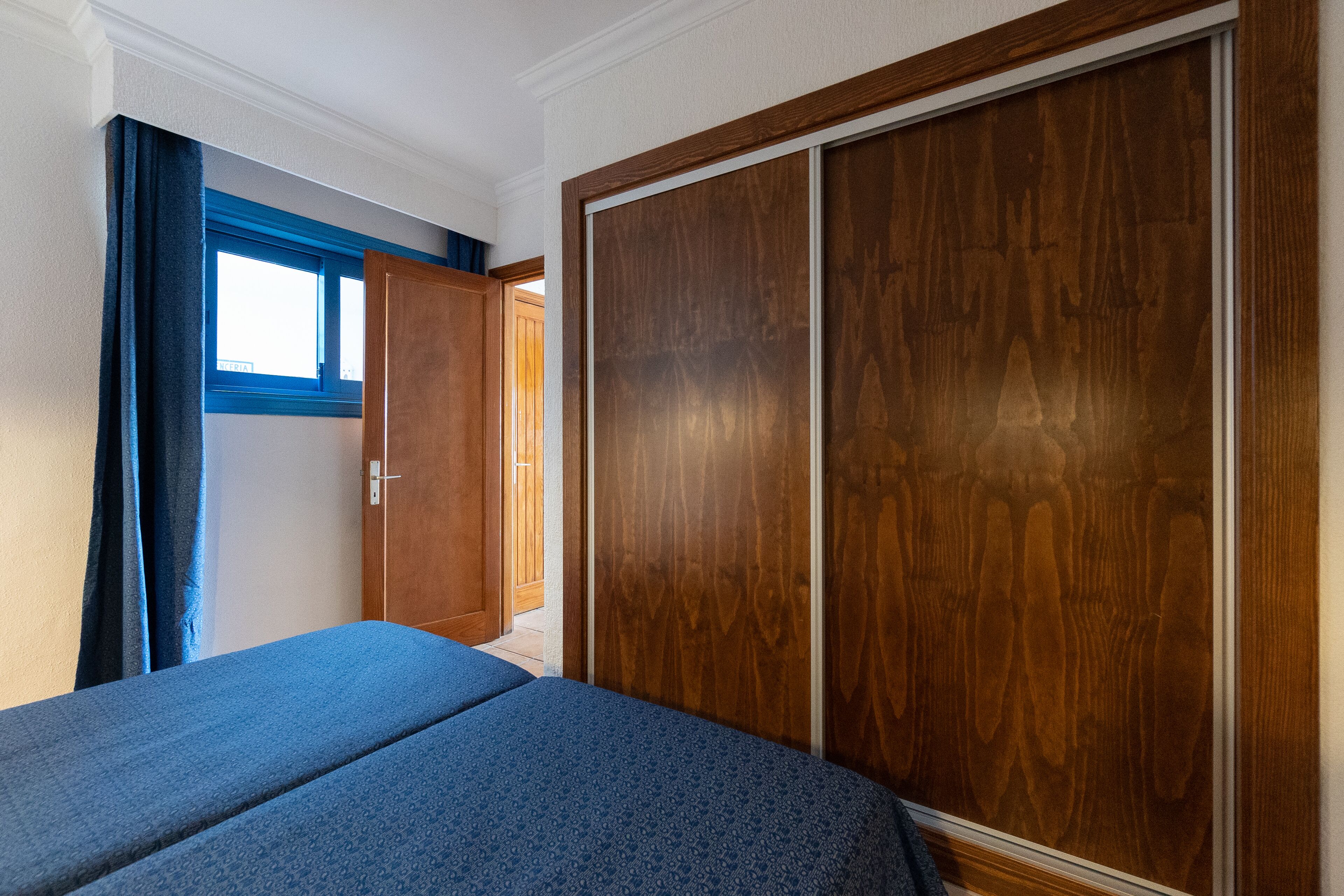 Un dormitorio con un armario grande, una cama con cubrecama azul y una ventana con cortinas azules.