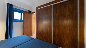 Un dormitorio con un armario grande, una cama con cubrecama azul y una ventana con cortinas azules.