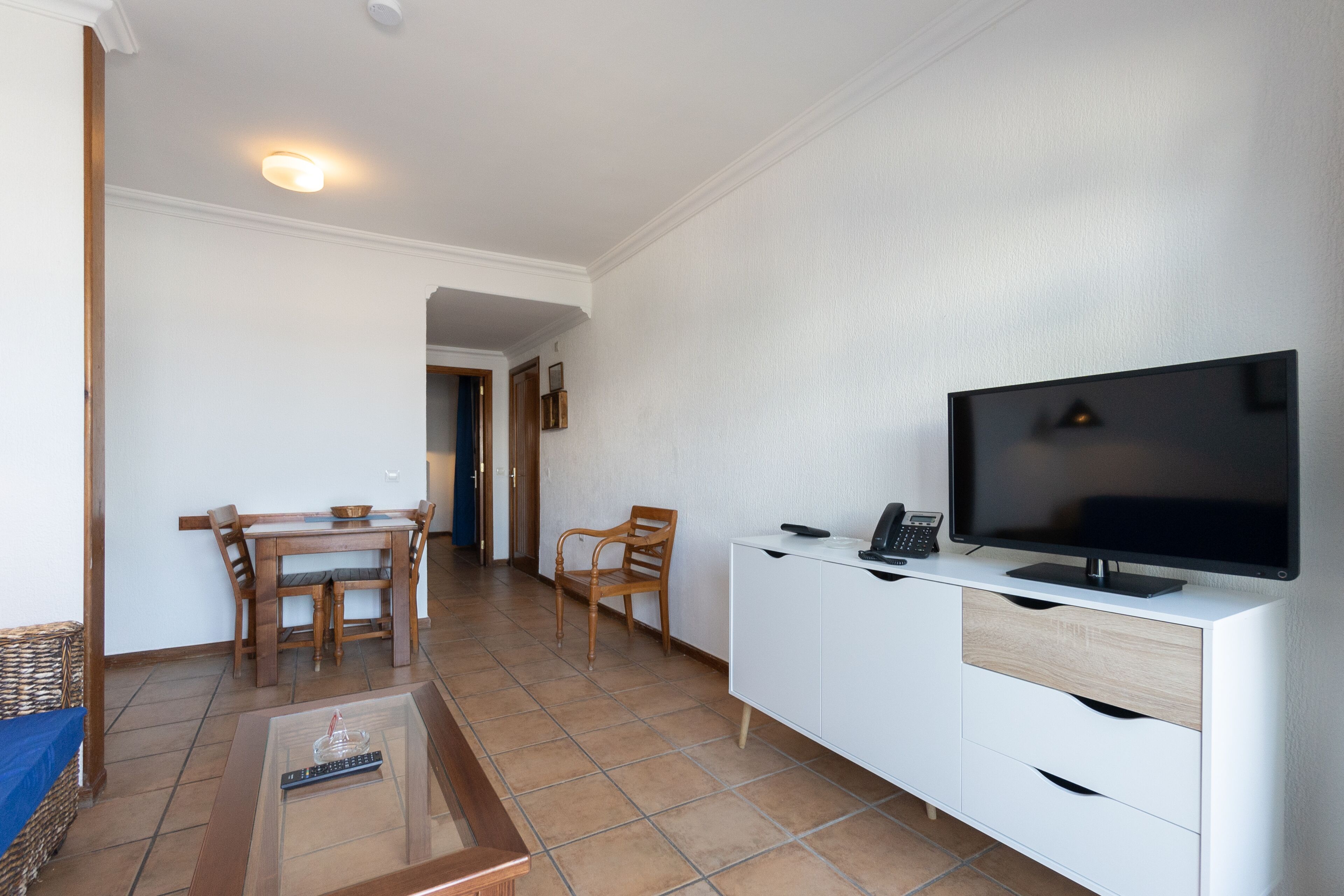 A living room with a TV, a dining table, chairs, and a white cabinet.