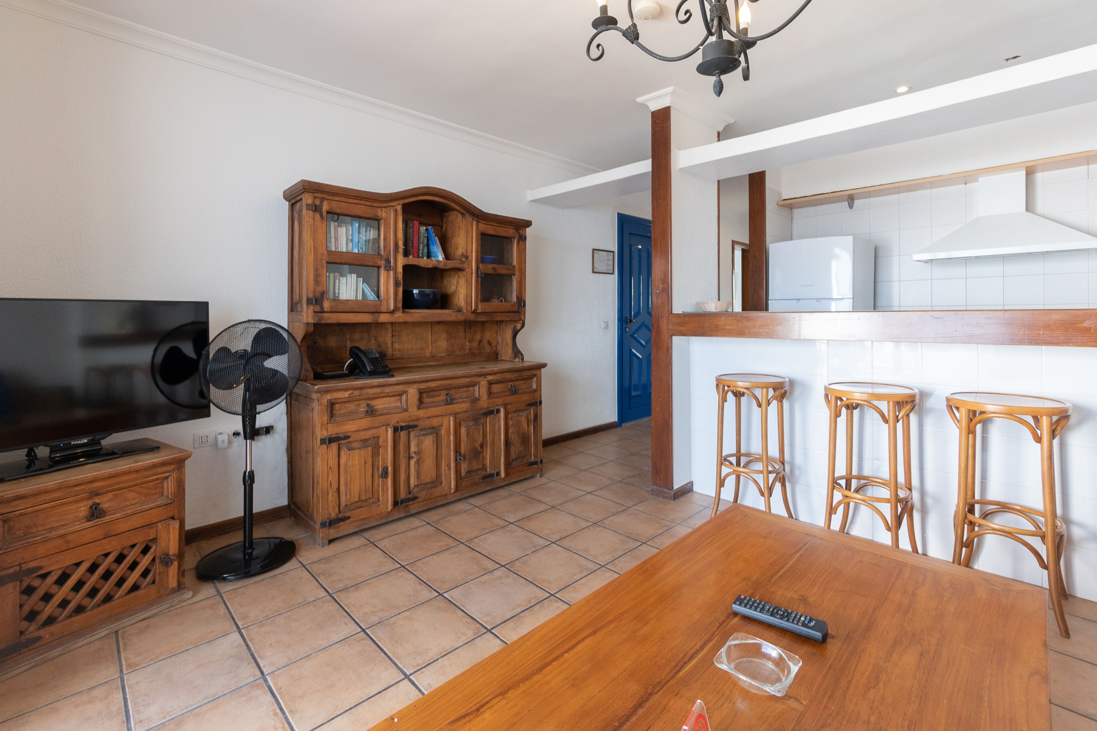 A dining area with a wooden table, bar stools, a television, and a wooden cabinet with glass doors.