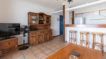 A dining area with a wooden table, bar stools, a television, and a wooden cabinet with glass doors.