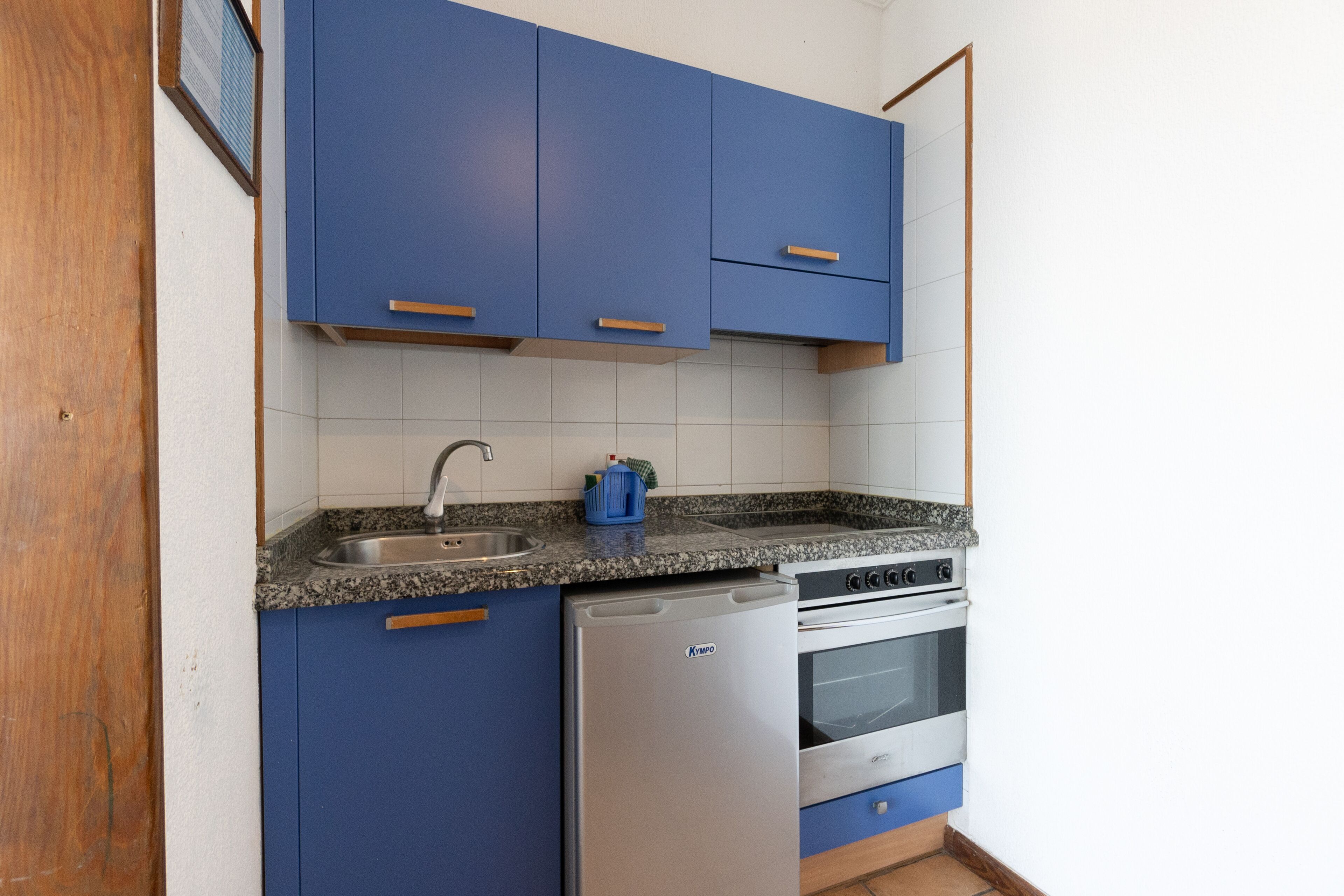 Cocina compacta con alacenas azules, pileta de acero inoxidable, lavavajillas y horno integrado.