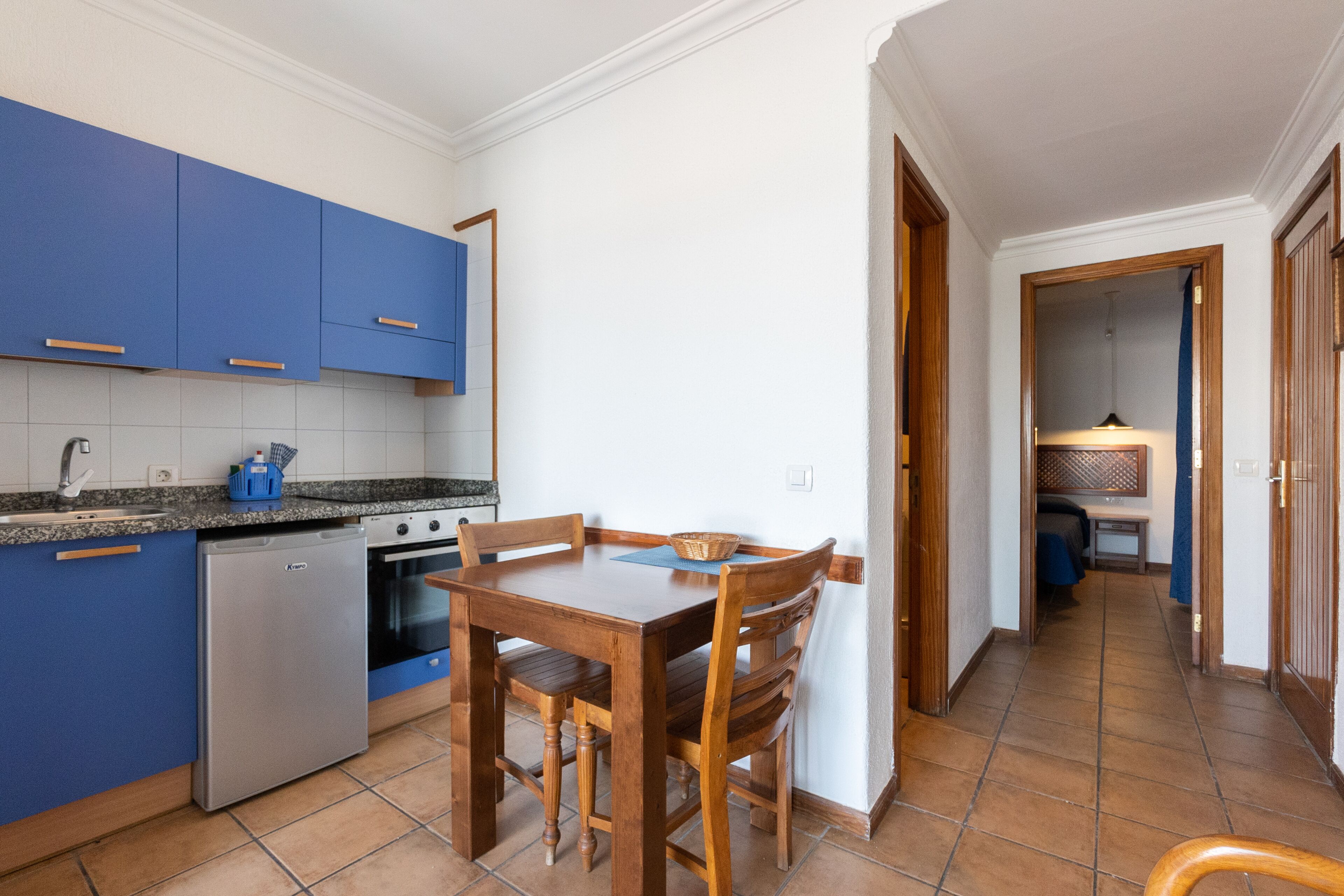 Una cocina compacta con armarios azules, una mesa de comedor con sillas y un horno a la vista.