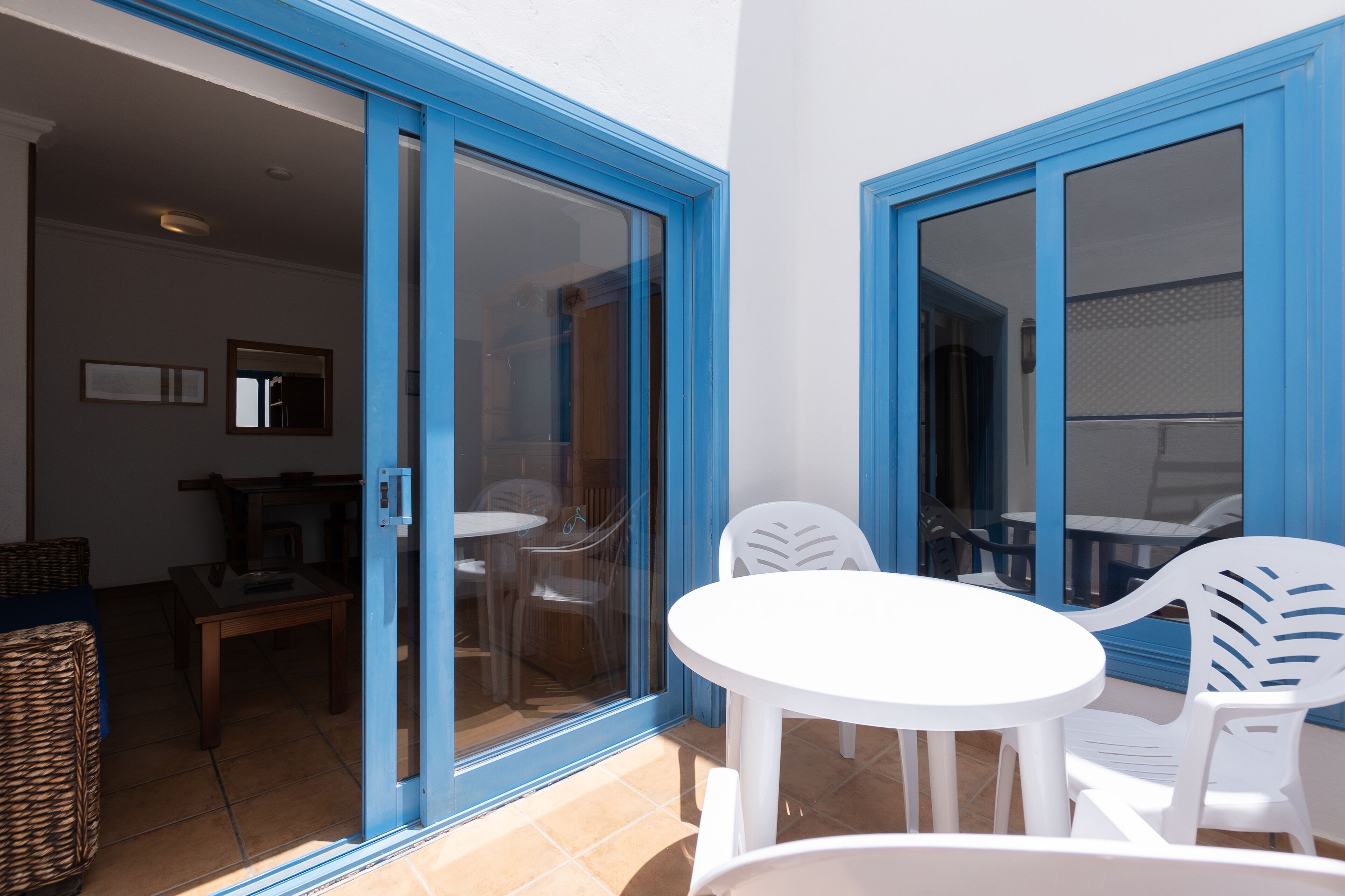 A patio area with a white table and chairs, a wicker basket, and a glass door leading to an indoor space.