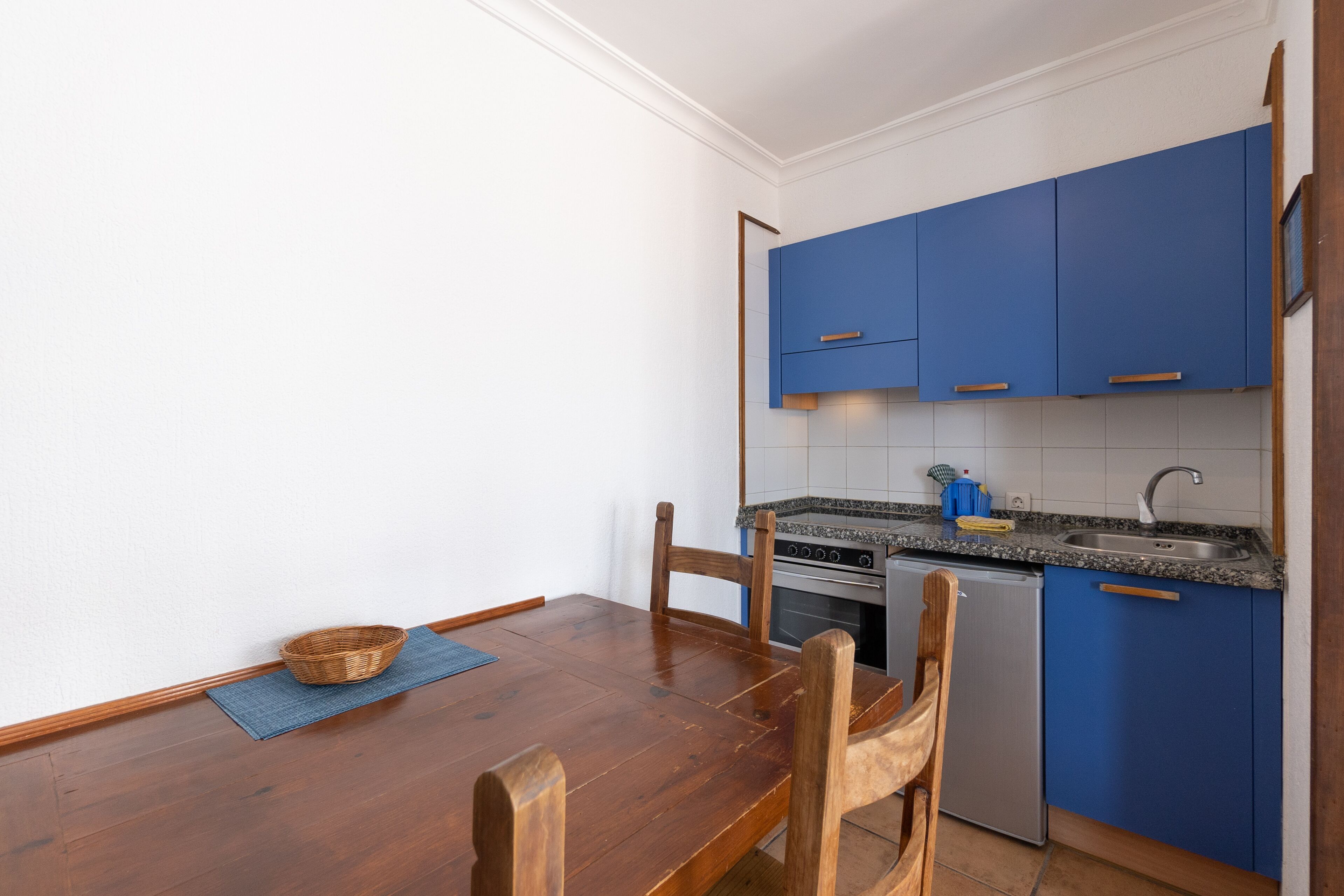 A compact kitchen with blue cabinets, a wooden dining table, and a small sink.