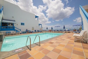 Una piscina al aire libre, sombrillas, sillones reclinables de piscina