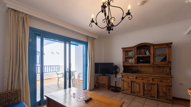 A living room with a wooden coffee table, a television, a bookshelf, and a balcony with a view. - Apartments Agua Marina (Tías)